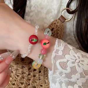 Primo piano di braccialetti estivi con perline e ciondoli a forma di mela e pesca.