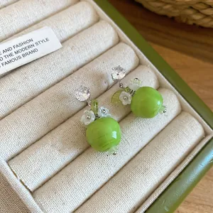 Primo piano di orecchini a lobo a forma di mela verde con dettagli in zircone e fiori.