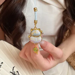 Close-up of a lucky cat pendant with a lollipop charm and fabric embroidery.