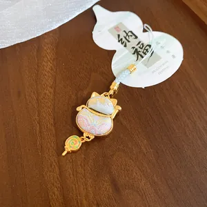 Close-up of a lucky cat charm with a colorful lollipop pendant on a wooden surface.