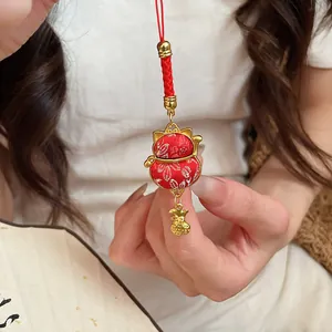 Close-up of a red lucky cat blessing bag charm with gold floral patterns and metal accents