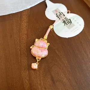 Detailed macro view of a pink brocade lucky charm pendant with cat ears and paw charm