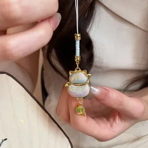 Detailed view of a lucky cat bag pendant with brocade fabric and a tiny lollipop charm