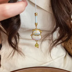 Close-up of maneki-neko lucky cat charm with rainbow lollipop pendant and woven cord.