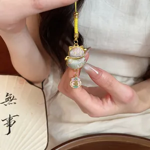 Close-up of a cute lucky cat charm with intricate floral patterns and yellow woven cord.