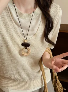 Detail view of a vintage bohemian woven long necklace styled on a beige knit sweater.