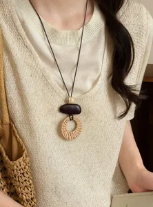 Detail of ethnic long necklace with woven rattan pendant worn on beige knit vest