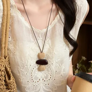 Detailed view of bohemian woven long necklace with dark brown pendant on white embroidered top.