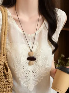 Bohemian long necklace with woven beads and dark stone pendant on a white lace top.