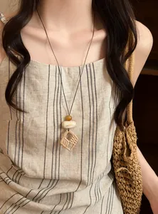 Close-up of bohemian style woven geometric pendant necklace on a model wearing linen dress
