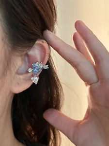 Primo piano di un ear cuff con zirconi a forma di uva e cuore indossato sull'orecchio