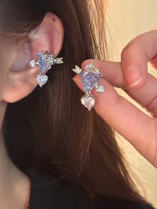 Primo piano dettagliato di un orecchino a clip a uva viola con zircone a forma di cuore.