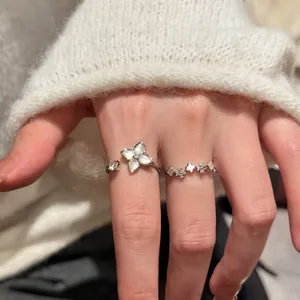 Gros plan d'élégantes bagues fleur en nacre portées sur une main avec un pull blanc
