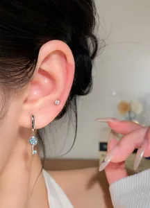Close-up of elegant silver key pendant earrings with blue zircons on ear