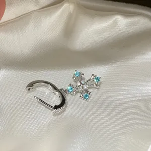 Silver cross dangle earring with blue and white cubic zirconia on white satin