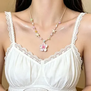 Detalle de un collar de cuentas colorido con un colgante de flor rosa en una modelo.