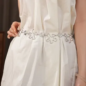 Détail d'une chaîne de taille en métal argenté avec fleurs évidées sur robe blanche