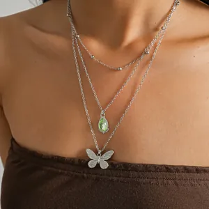 Collier multi-rangs en acier inoxydable avec goutte verte et pendentif papillon porté au cou.