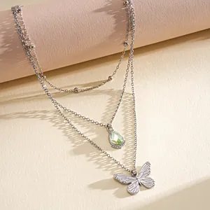 Détail rapproché du collier multicouche en acier avec goutte verte et pendentif papillon