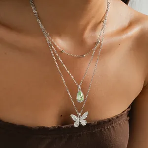 Gros plan d'un collier multi-rangs en acier inoxydable avec pendentifs papillon et goutte verte.