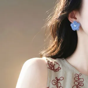 Détail macro d'une boucle d'oreille fleur en perles bleues portée par un mannequin