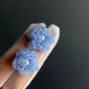 Vue détaillée de boucles d'oreilles fleurs en perles bleues avec une perle blanche.