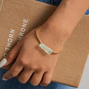 Dettaglio di un bracciale rigido dorato minimalista con pietra di cristallo verde