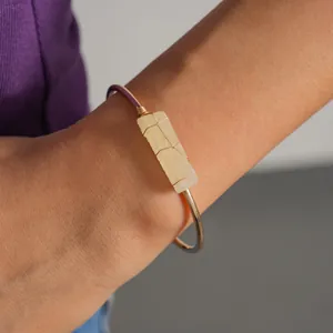 Dettaglio di un bracciale dorato con una pietra naturale gialla avvolta in filo metallico.