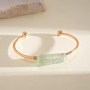 Dettaglio di bracciale rigido oro rosa con cristallo verde grezzo avvolto.