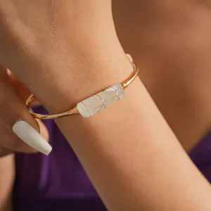 Vista dettagliata di una pietra di cristallo bianco irregolare su un bracciale rigido dorato