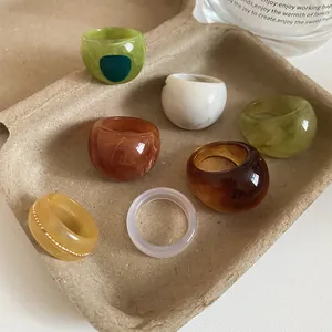Group of colorful marbled resin rings with irregular textures and glossy finish in a tray.