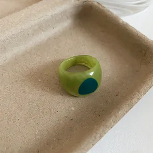 Close-up of a green transparent resin ring with an irregular textured finish and blue dot.