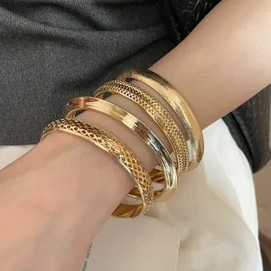 Detailed view of gold-toned irregular matte hollow metal bangles set on a wrist.