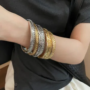 Detail view showing stacked gold and silver matte hollow-out bangles with irregular design.
