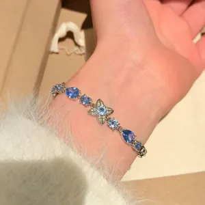 Close-up detail of a delicate silver bracelet with blue gemstones and a central flower charm.