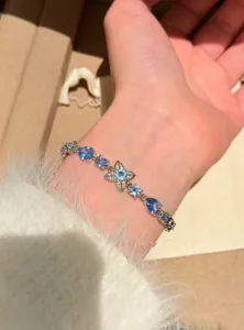 Detail shot of a delicate silver bracelet with blue gemstones and a floral charm.