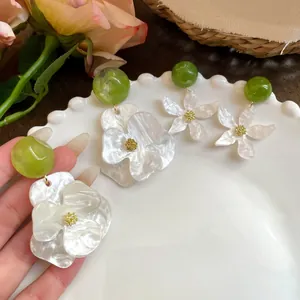 Detailed view of white acetate gardenia floral earrings with green ball studs on a white plate