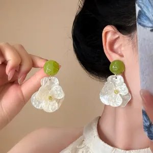 Detailed view of white gardenia flower earrings with green studs on model's ear
