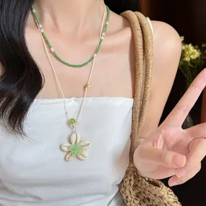 Detailaufnahme einer mehrlagigen grünen Perlenkette mit einem Muschel-Blumen-Anhänger