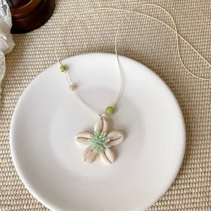 Nahaufnahme einer Muschelblumen-Halskette mit grüner Perlenmitte und Schnur.