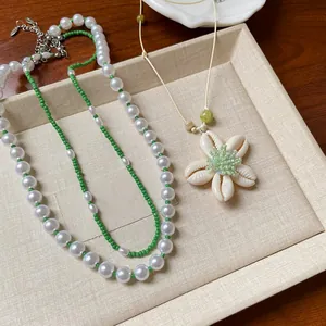 Detail einer weißen Perlen- und grünen Perlenkette mit einem Muschelblumenanhänger.