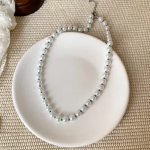 Nahaufnahme einer eleganten weißen Perlenkette mit grünen Zwischenperlen auf Keramikteller