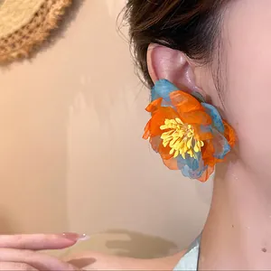 Close-up detail of oversized orange and blue layered chiffon flower stud earrings on model