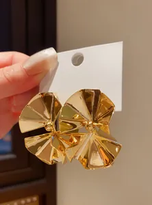 Close-up detail of large gold geometric folded stud earrings with high-gloss metallic finish.