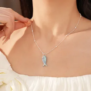 Detailopname van een zilveren kralenketting met een opalen vishanger op een model