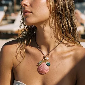 Close-up of a pink shell pendant necklace with pearl charms on a sun-kissed beach.