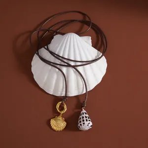 Detail shot of a shell necklace with gold and natural pendants on a shell prop.