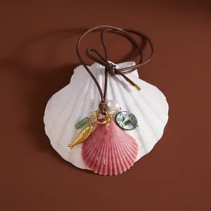 Detailed view of the shell necklace charms including a pink shell, gold fish, and pearl.