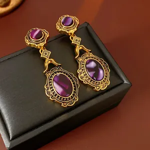 Detailed view of vintage gold-tone drop earrings with purple stones on a black gift box