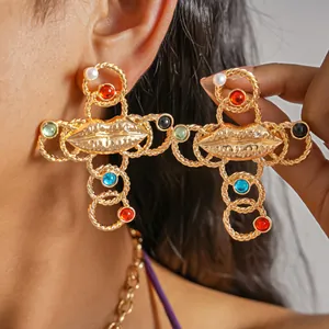 Detail of vintage golden cross earrings with lip motif and colorful resin beads.
